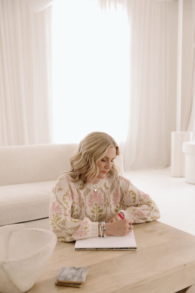 Molly Rubesh journaling at a sunlit table, reflecting on finding joy in the present moment.