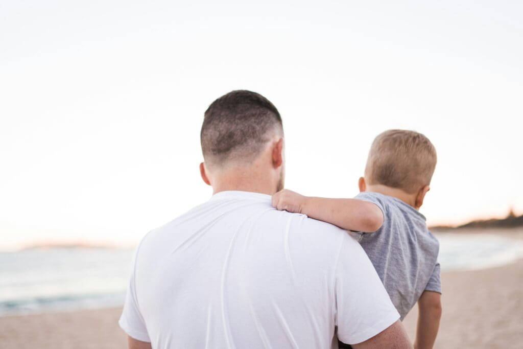 A father holding his toddler son at the beach.